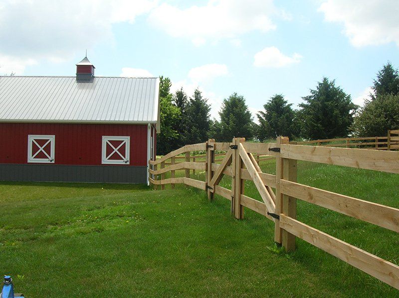 Red barn with white roof beside a wooden fence in a sunny grassy field