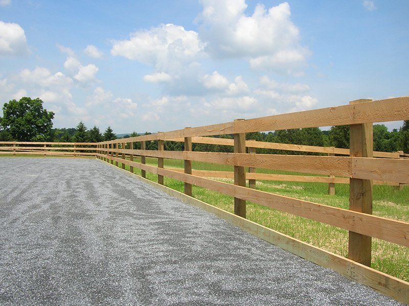 Gravel path beside wooden fence in a sunny rural field under a partly cloudy sky