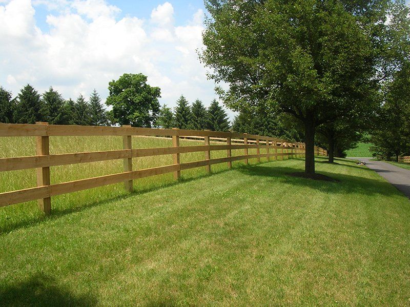 Wooden fence beside a green grassy field and road under a partly cloudy sky
