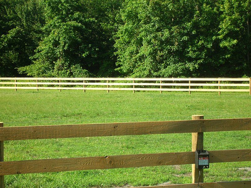 Wooden fence in a green grassy field with trees in the background