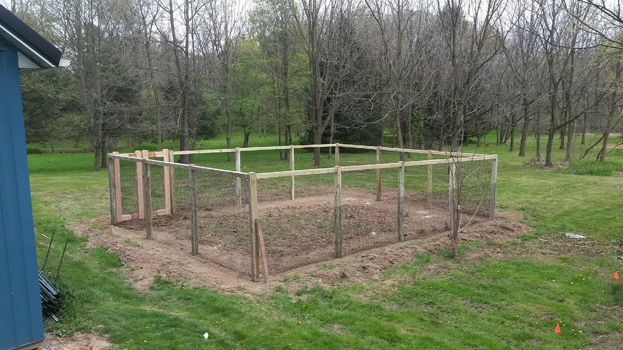Wooden garden bed frame in a grassy yard with bare soil, surrounded by trees.