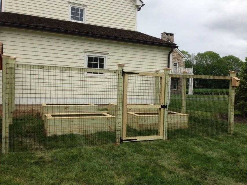 Wooden chicken coop and fenced run beside a white house on a grassy lawn.