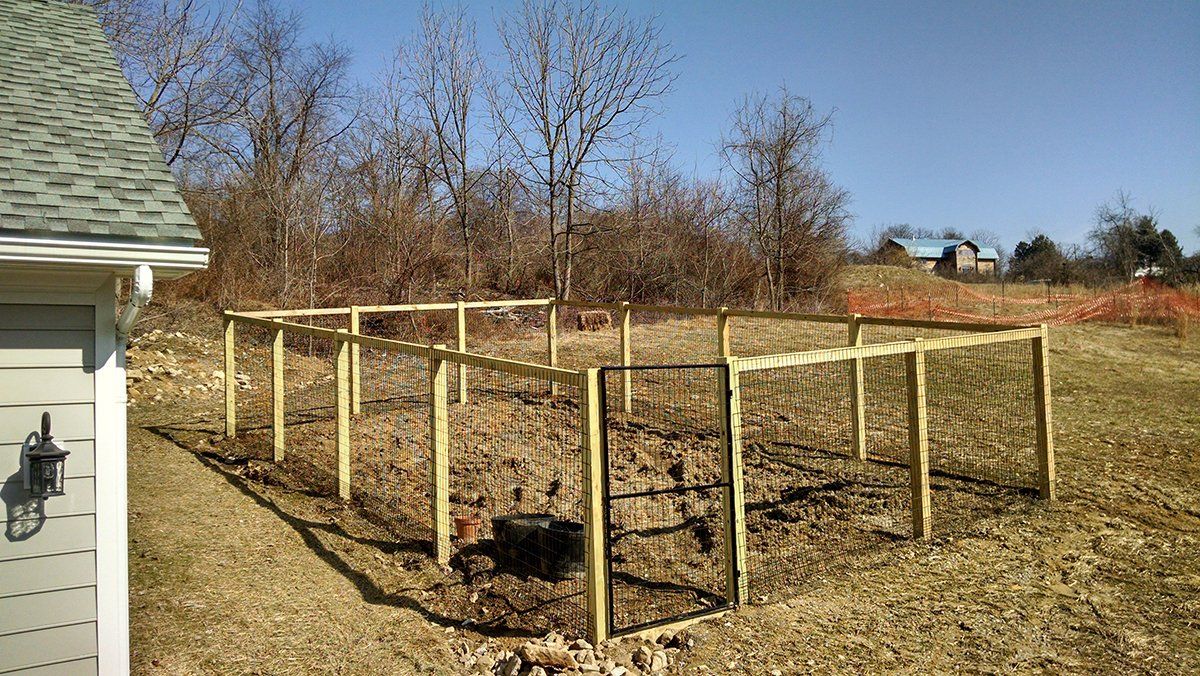 Wooden fence posts outlining a garden bed beside a house in a leaf-covered yard under a blue sky
