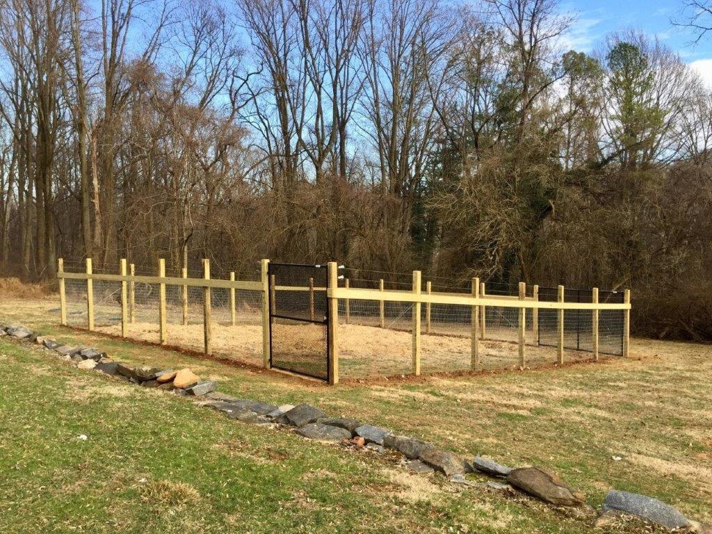 Wooden fenced enclosure in a grassy yard with trees in the background