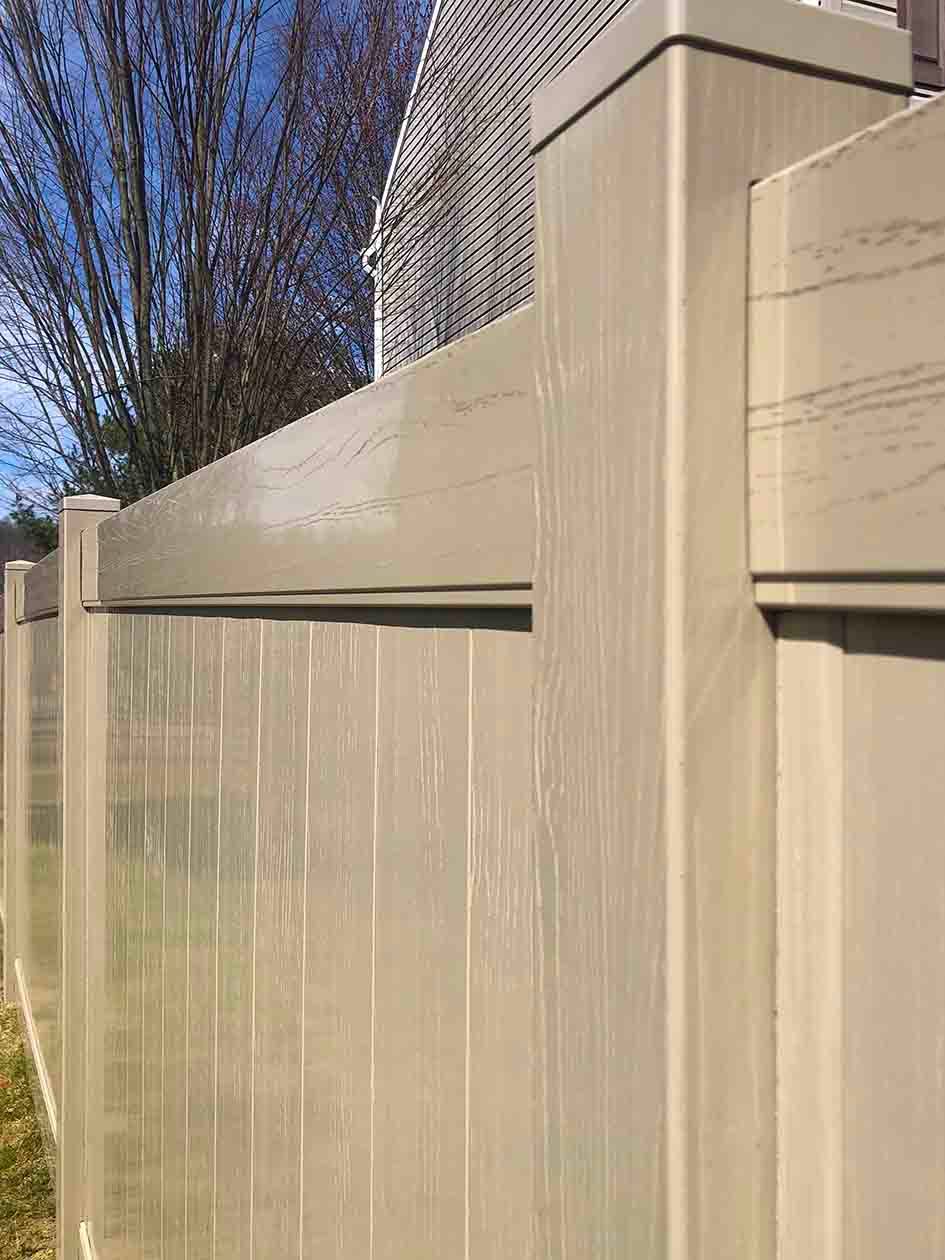 Tall beige fence with water streaks beside a building under a blue sky