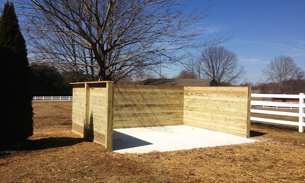 Small outdoor wood-and-concrete enclosure in a yard, with white fence and leafless trees behind it