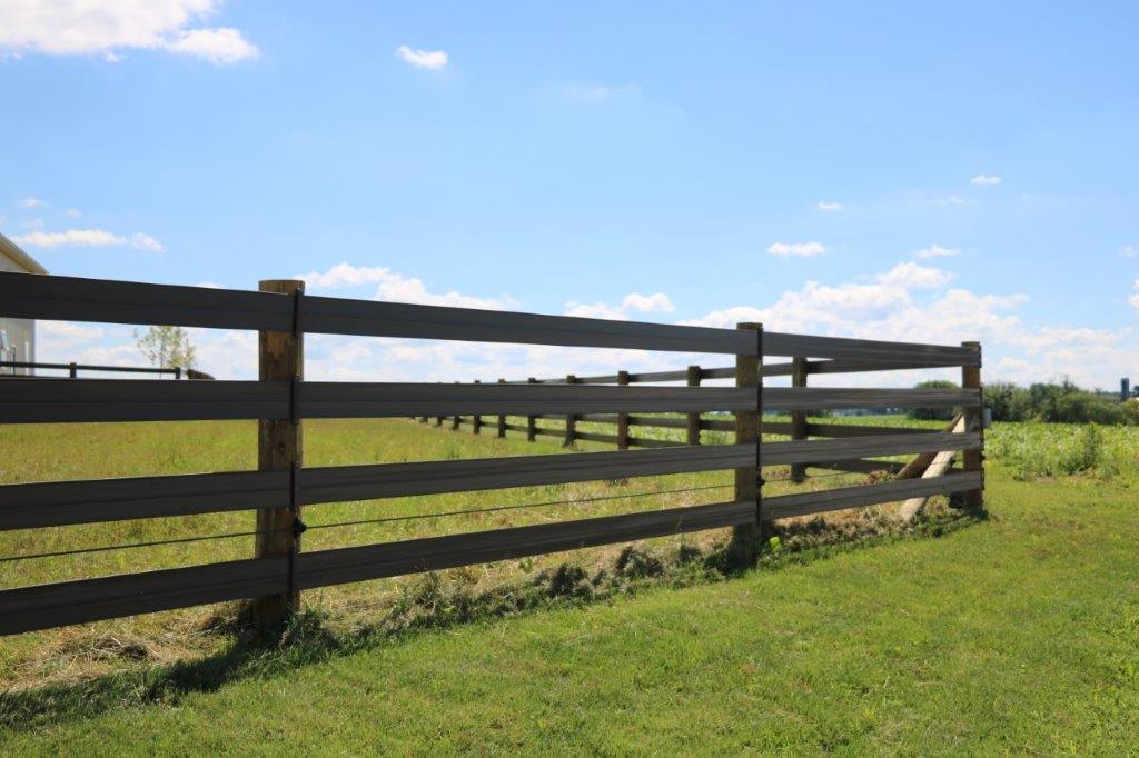 Wooden split-rail fence beside a grassy field under a blue sky with clouds