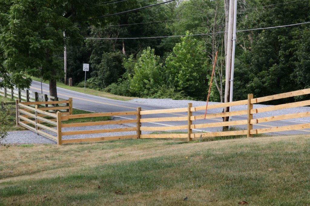 Wooden fence along a rural road with trees and grass beyond it