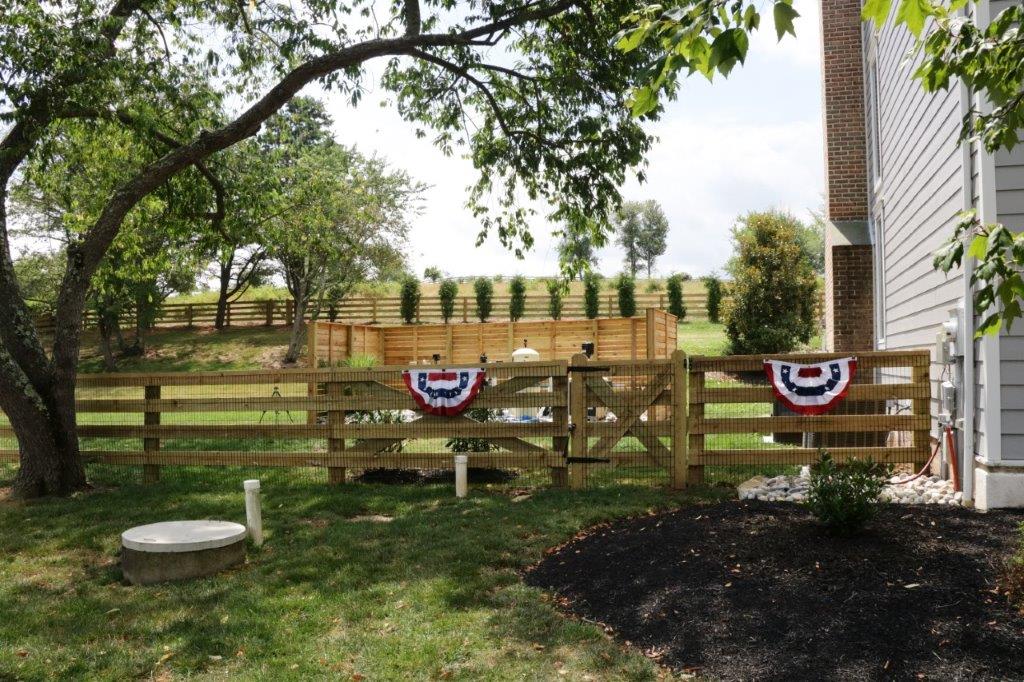 Backyard fence with patriotic bunting, tree shade, and a house beside a mulch bed