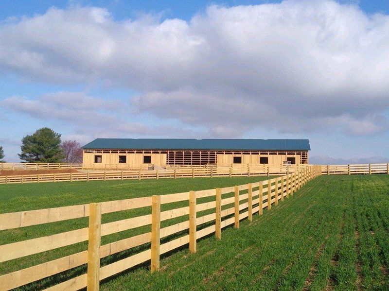 Rural farm buildings beside fenced green fields under a cloudy sky