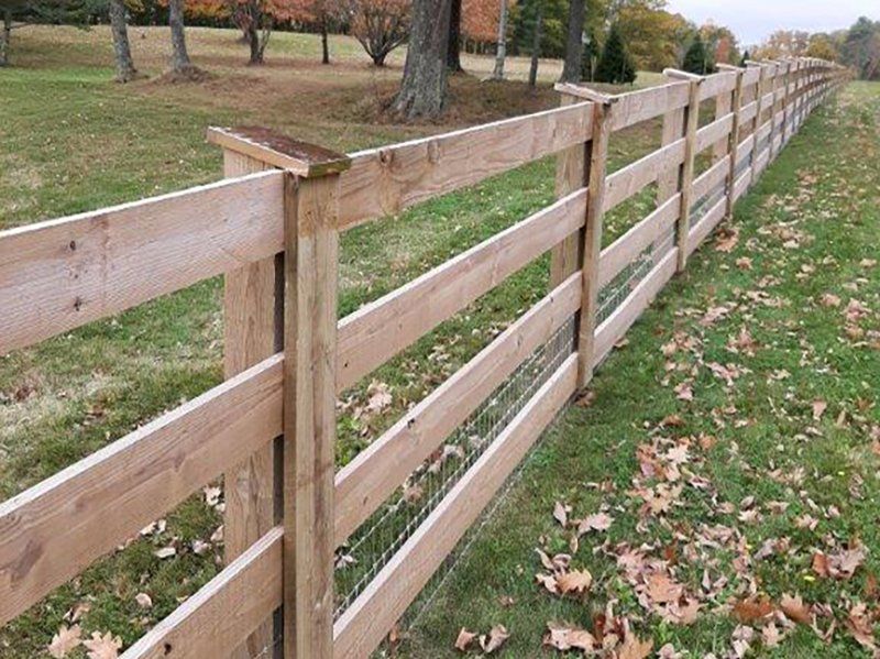 Wooden split-rail fence along a grassy path with fallen autumn leaves