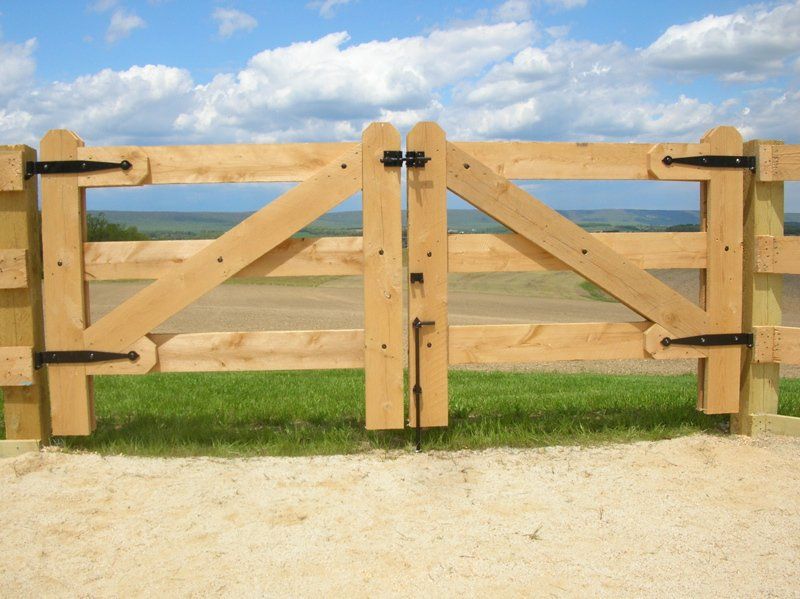 Wooden double gate with diagonal braces on a gravel path under a blue sky