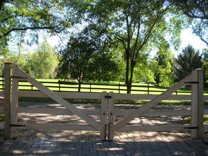 Wooden gate across a brick path, opening to a sunny park with trees and grass