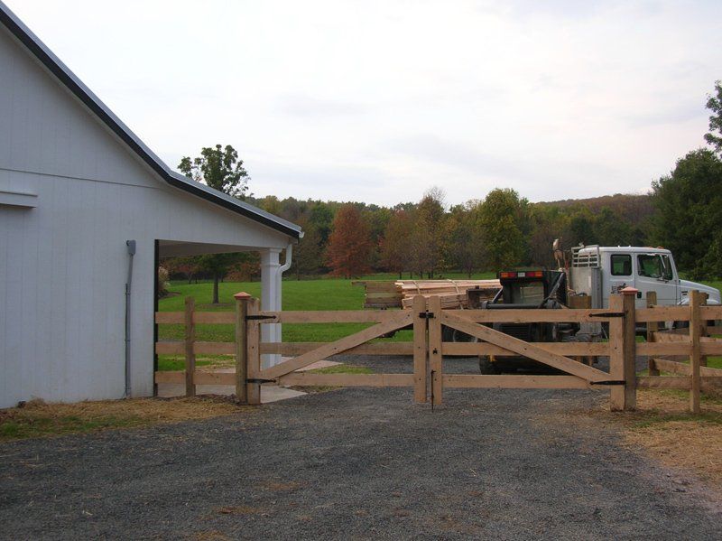 Barnyard gate beside white building, with gravel drive and parked truck in the background