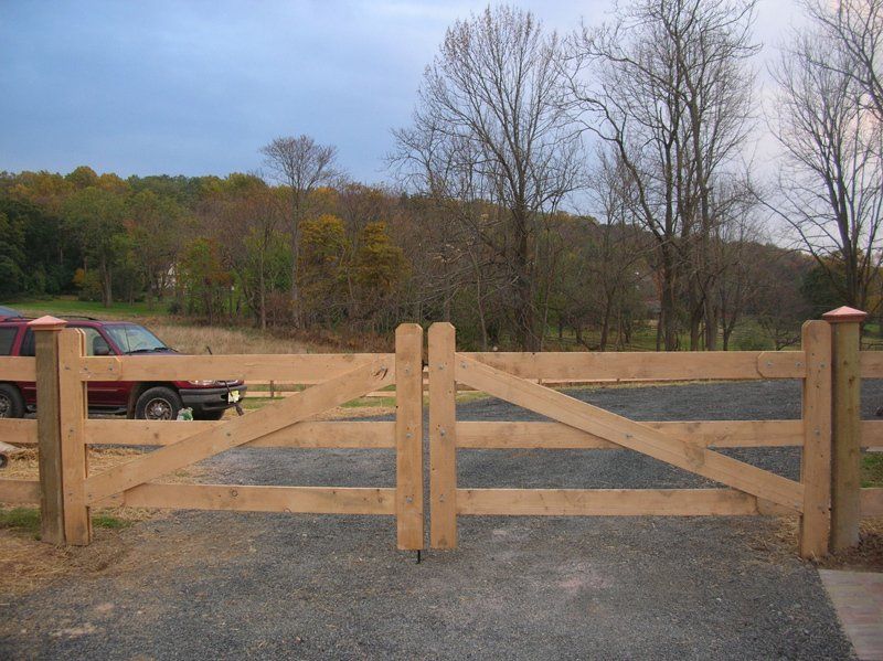 Wooden farm gate across a gravel driveway with a pickup truck and trees in the background