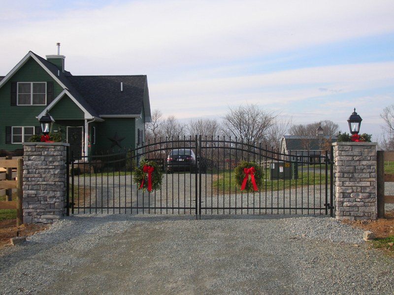 Black metal gate with red bows in front of a green house and gravel driveway