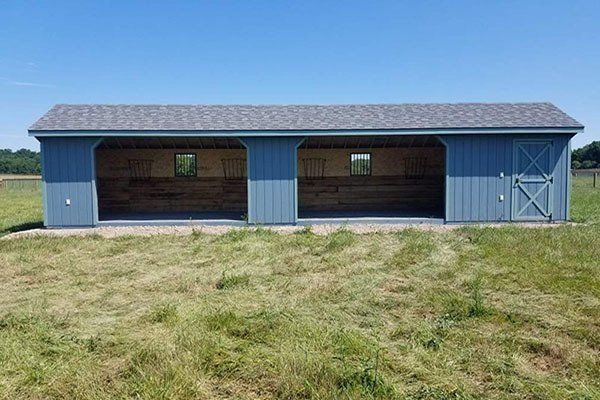 Blue barn-style shelter with two open bays and a grassy field in front, under a clear sky
