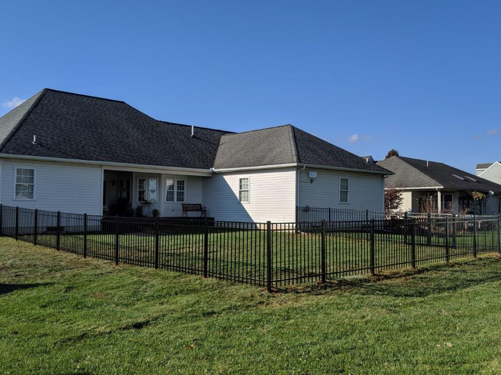 Single-story white house with dark roof and black fence on a grassy lawn under a blue sky