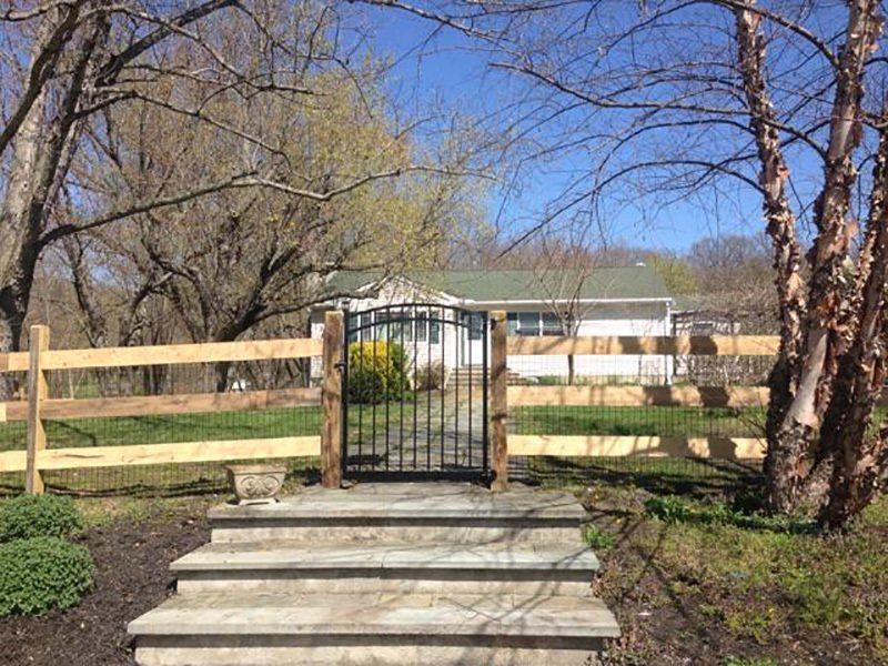 Stone steps leading to a black metal gate and fenced yard with a house and leafless trees behind