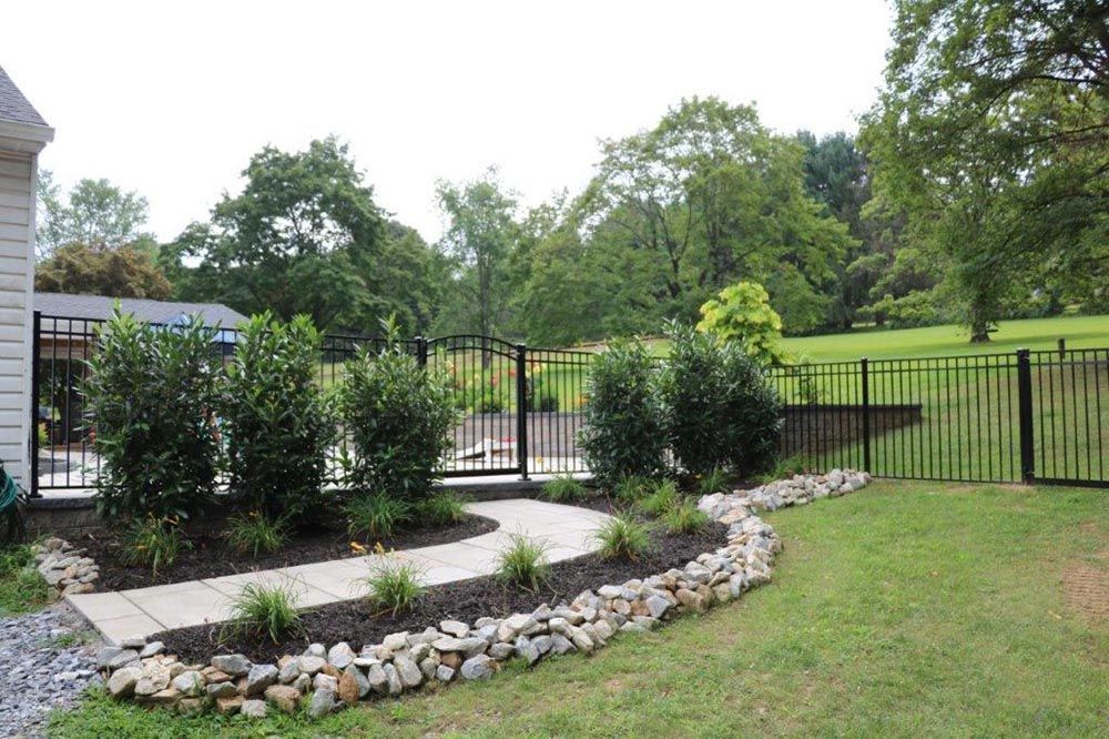 Landscaped backyard with stone flower bed, shrubs, black fence, and green lawn