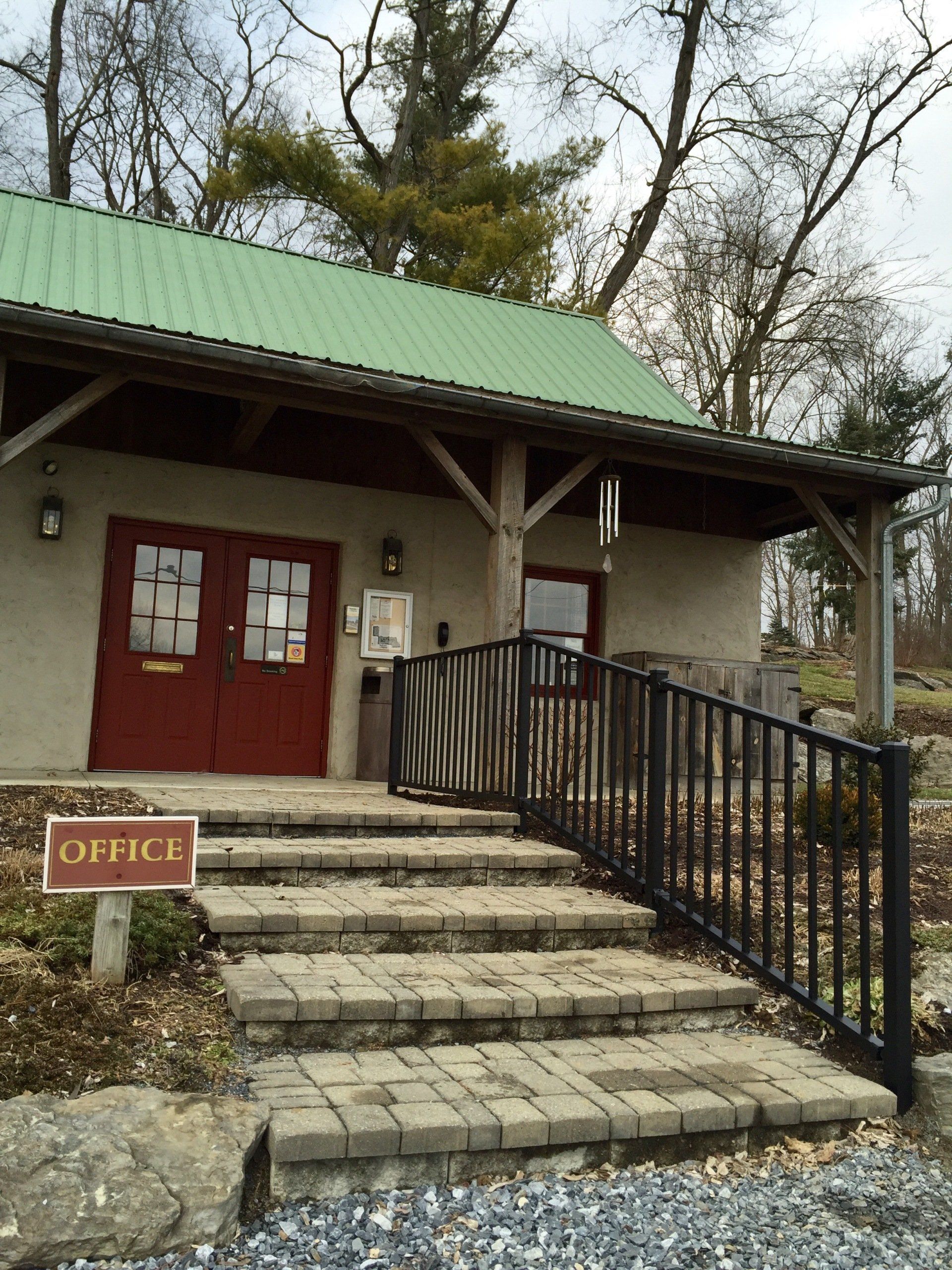 Stone steps lead to a red-doored office building with a green roof and black ramp railing