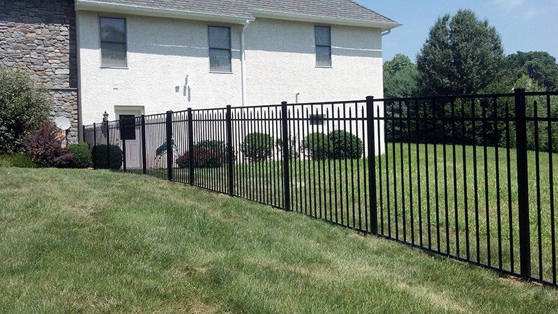 Black metal fence along a grassy yard beside a white house on a sunny day