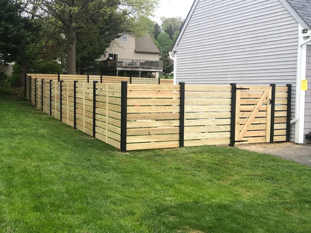 Wooden privacy fence enclosing a backyard beside a gray house on a green lawn