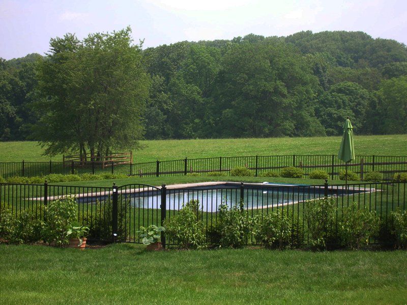 Fenced backyard pool with green lawn, trees, and wooded hills in the background