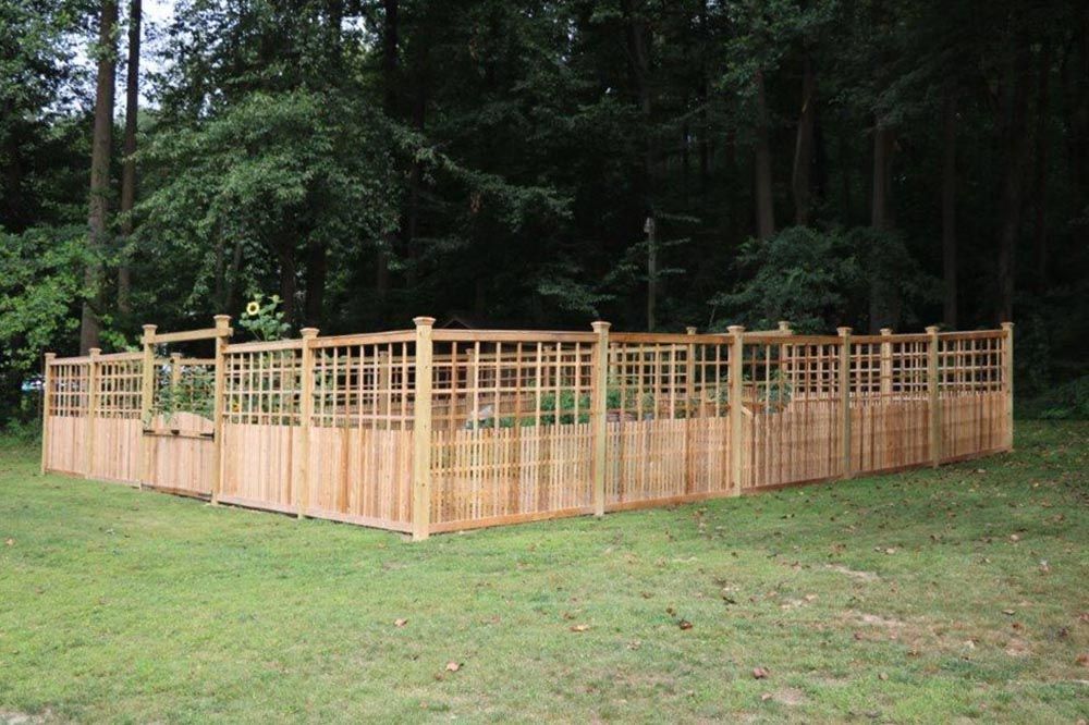 Wooden garden fence enclosing a grassy yard beside a wooded area