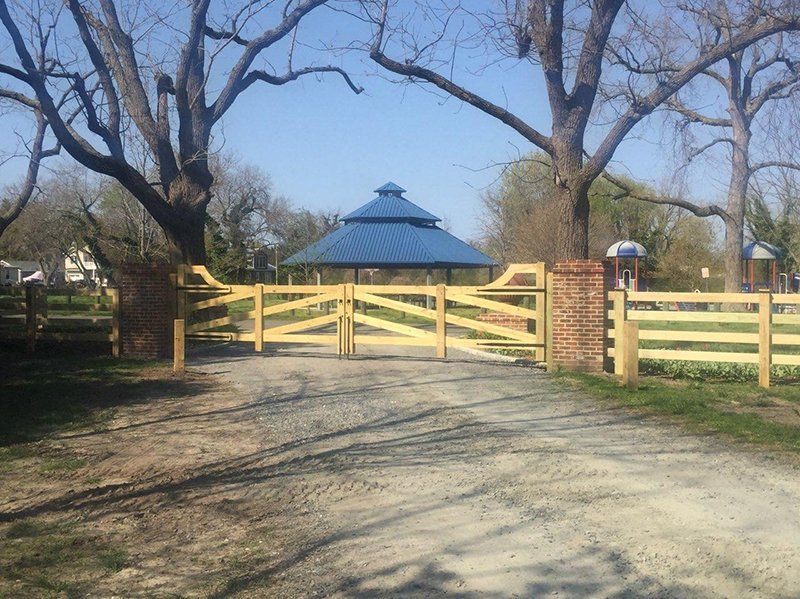 Yellow wooden gate and gravel driveway leading to a blue-roofed pavilion in a park with bare trees.