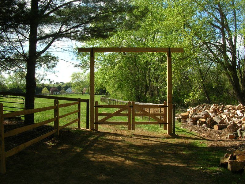 Wooden gate and fence at a sunny rural pasture entrance, with stacked firewood on the right