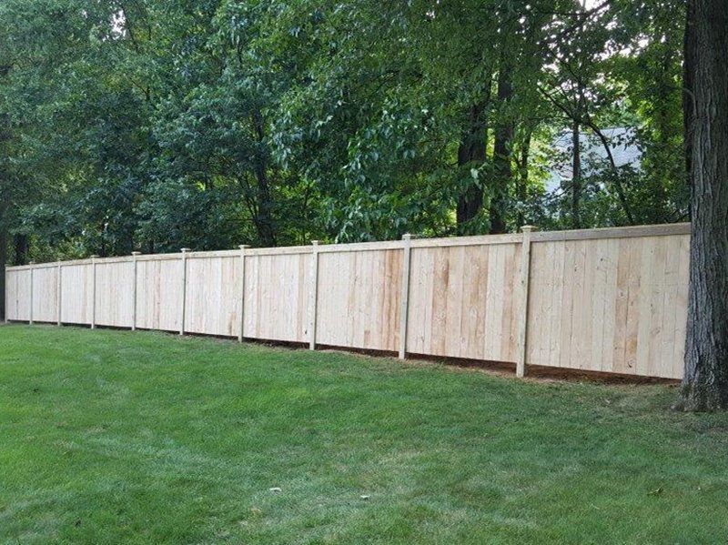 Long wooden fence beside a grassy yard with trees in the background