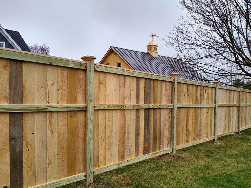 New wooden fence along a grassy yard with houses and bare trees in the background