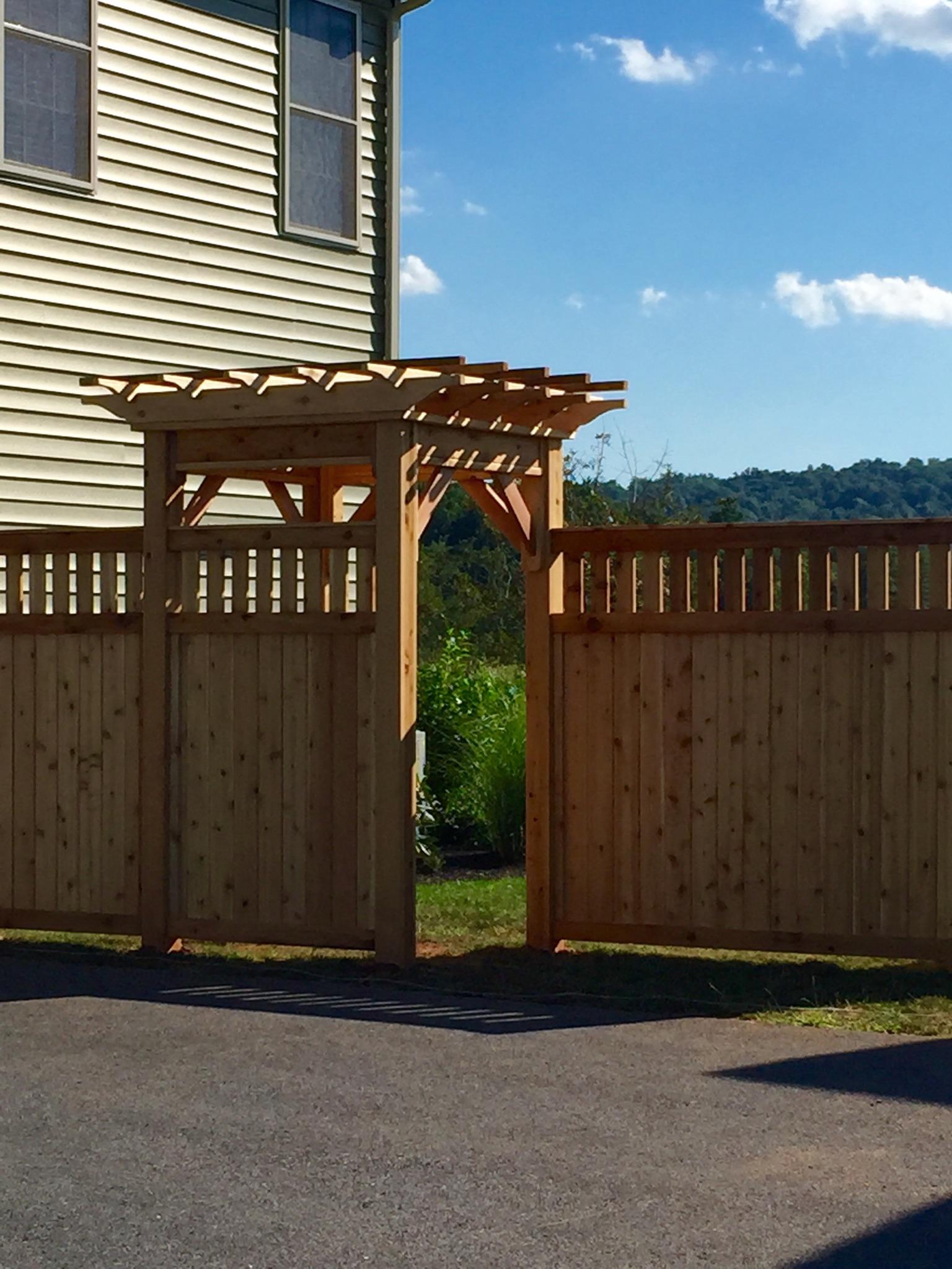 Wooden gate with trellis in a fenced backyard beside a house under a blue sky