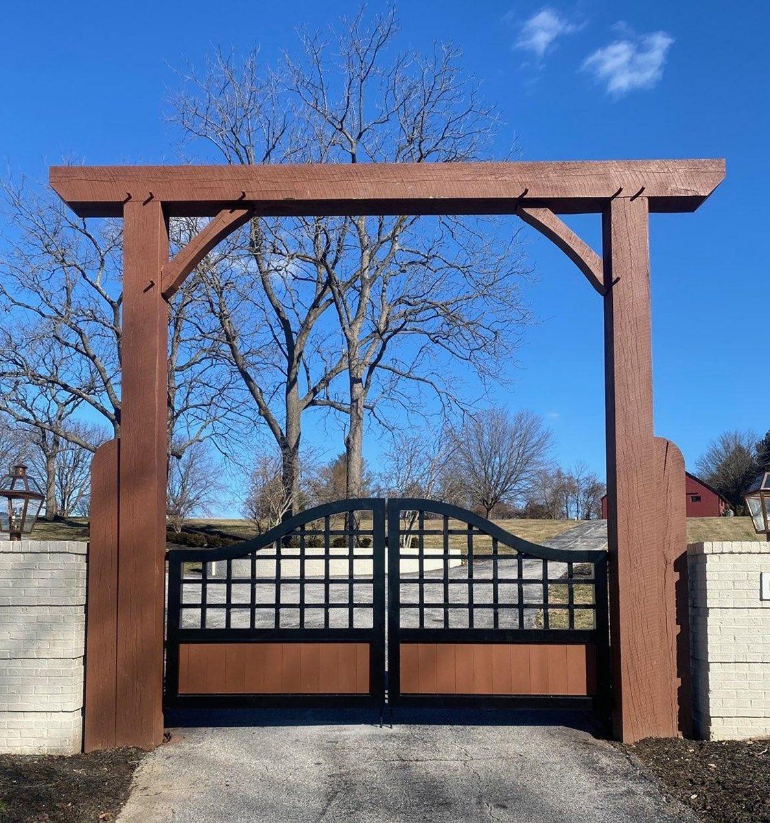 Wooden entrance arch with a black wrought-iron gate against a stone wall and blue sky
