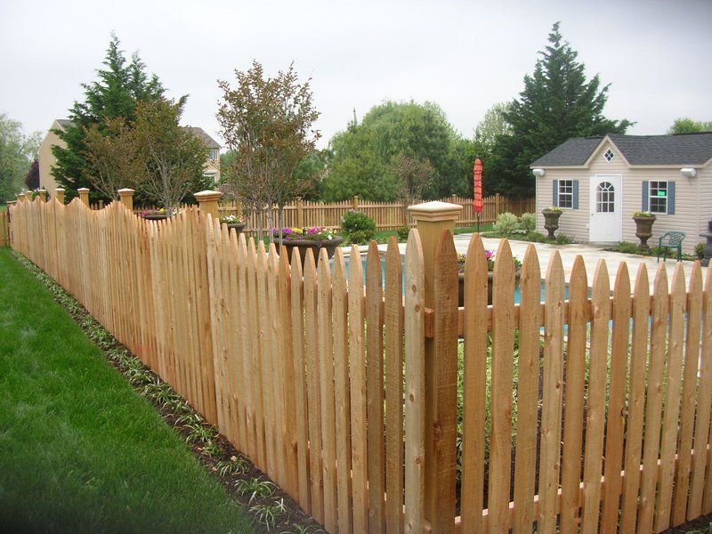 Wooden picket fence along a grassy yard with a house and trees in the background
