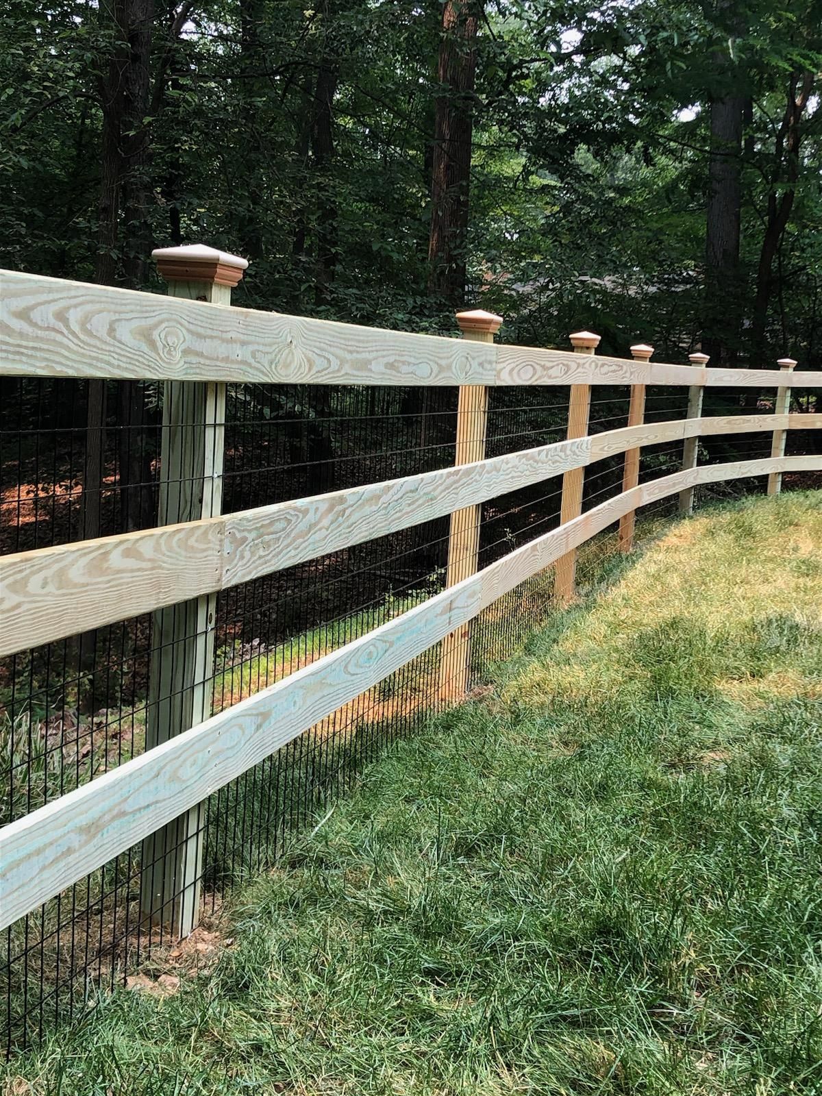 Wooden fence along a grassy path beside a wooded area