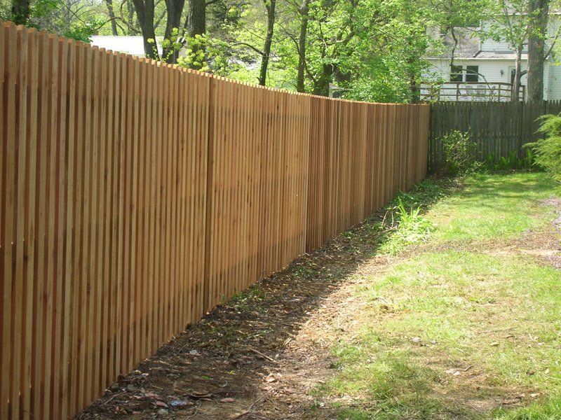 Wooden fence along a grassy path in a sunlit backyard with trees and a house in the background