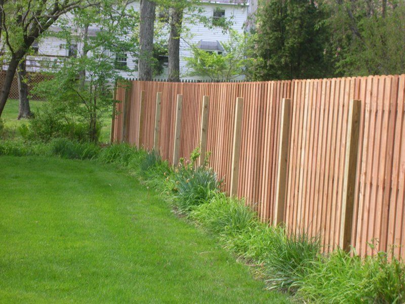 Green lawn beside a long wooden fence in a wooded yard