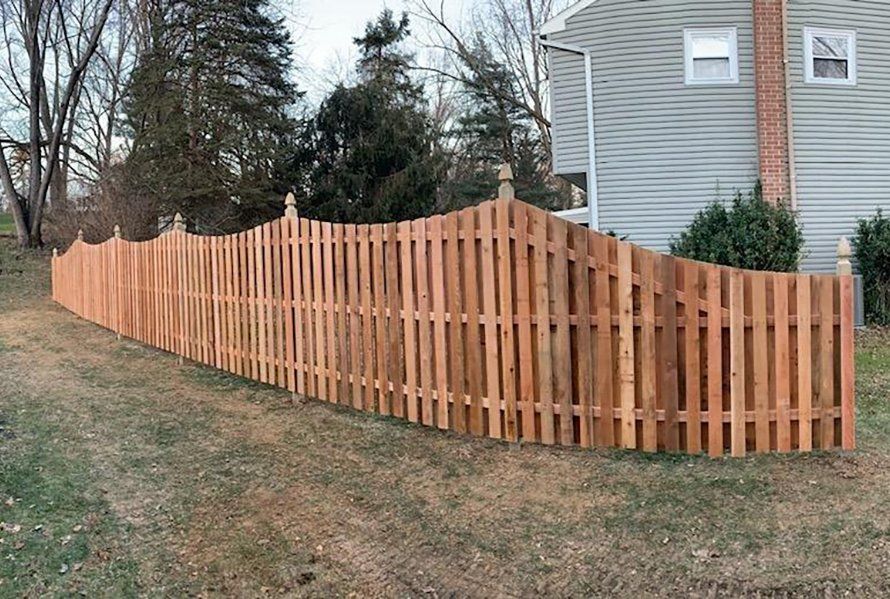 Curved wooden fence along a sloped yard beside a gray house in fall.