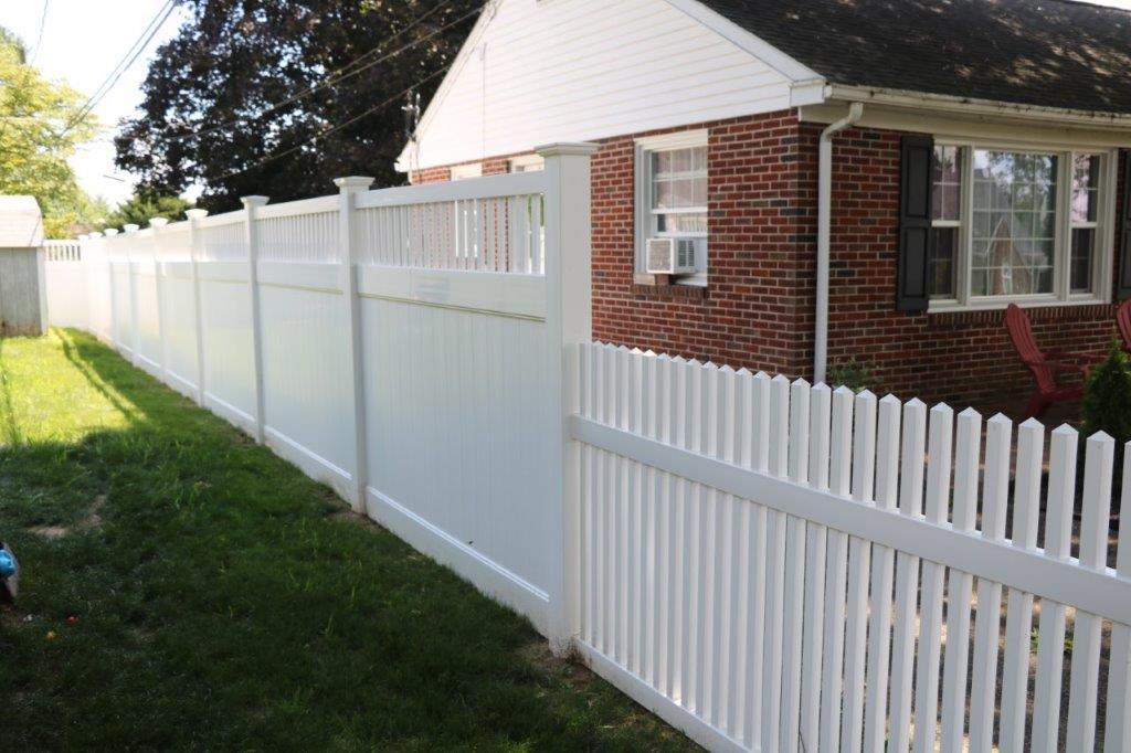 White picket fence along a grassy yard beside a brick house and white garage in daylight