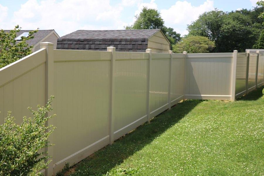 Beige vinyl privacy fence lining a grassy backyard with trees and a shed in the background