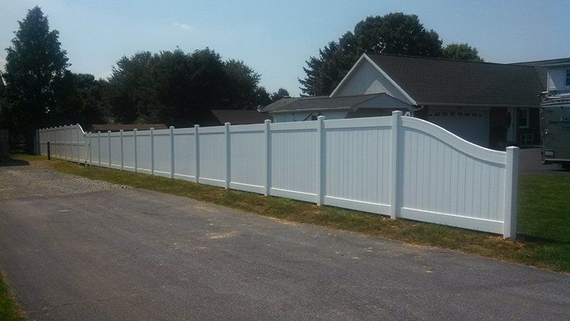 Long white vinyl fence along a driveway beside a house and trees.