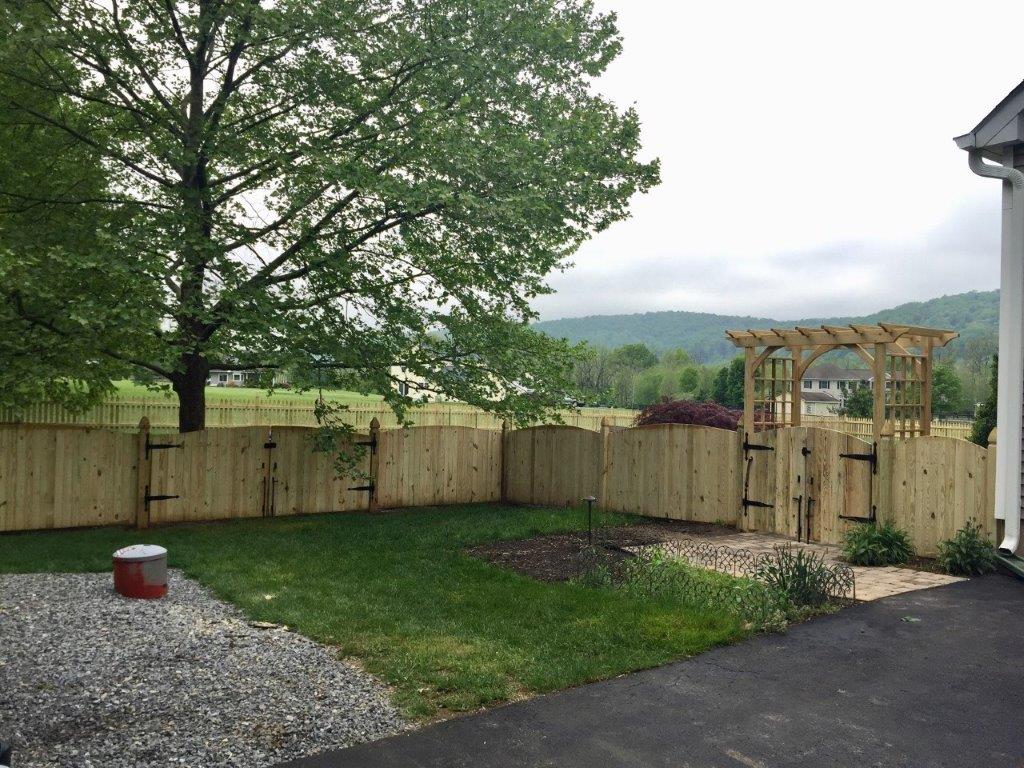 Backyard with wooden fence, tree, lawn, gravel drive, and mountain view beyond a gate