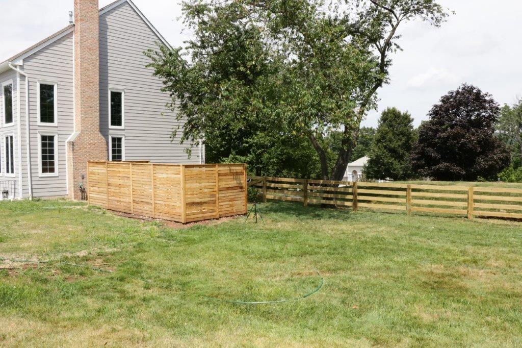 Backyard with a white house, wooden fence enclosure, and tree in a grassy yard