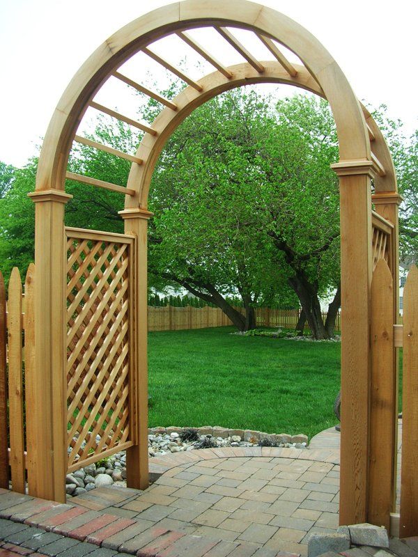 Wooden garden archway with lattice panels opening onto a grassy backyard and tree-filled view