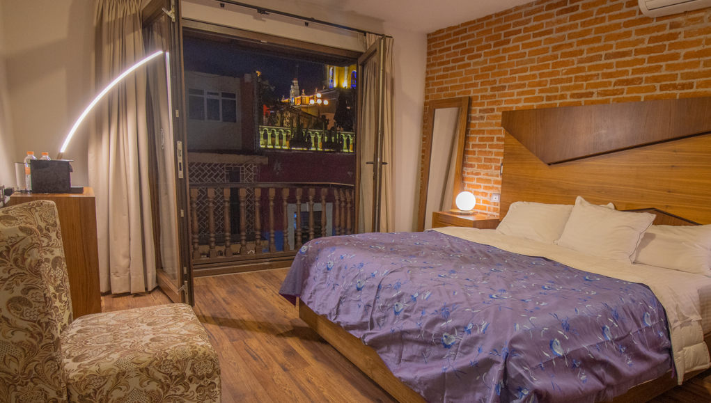 Un dormitorio con una cama grande, silla moderna y balcon con vista espectacular..