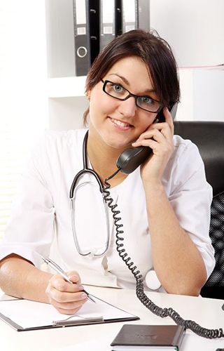 A female doctor is sitting at a desk talking on a phone.