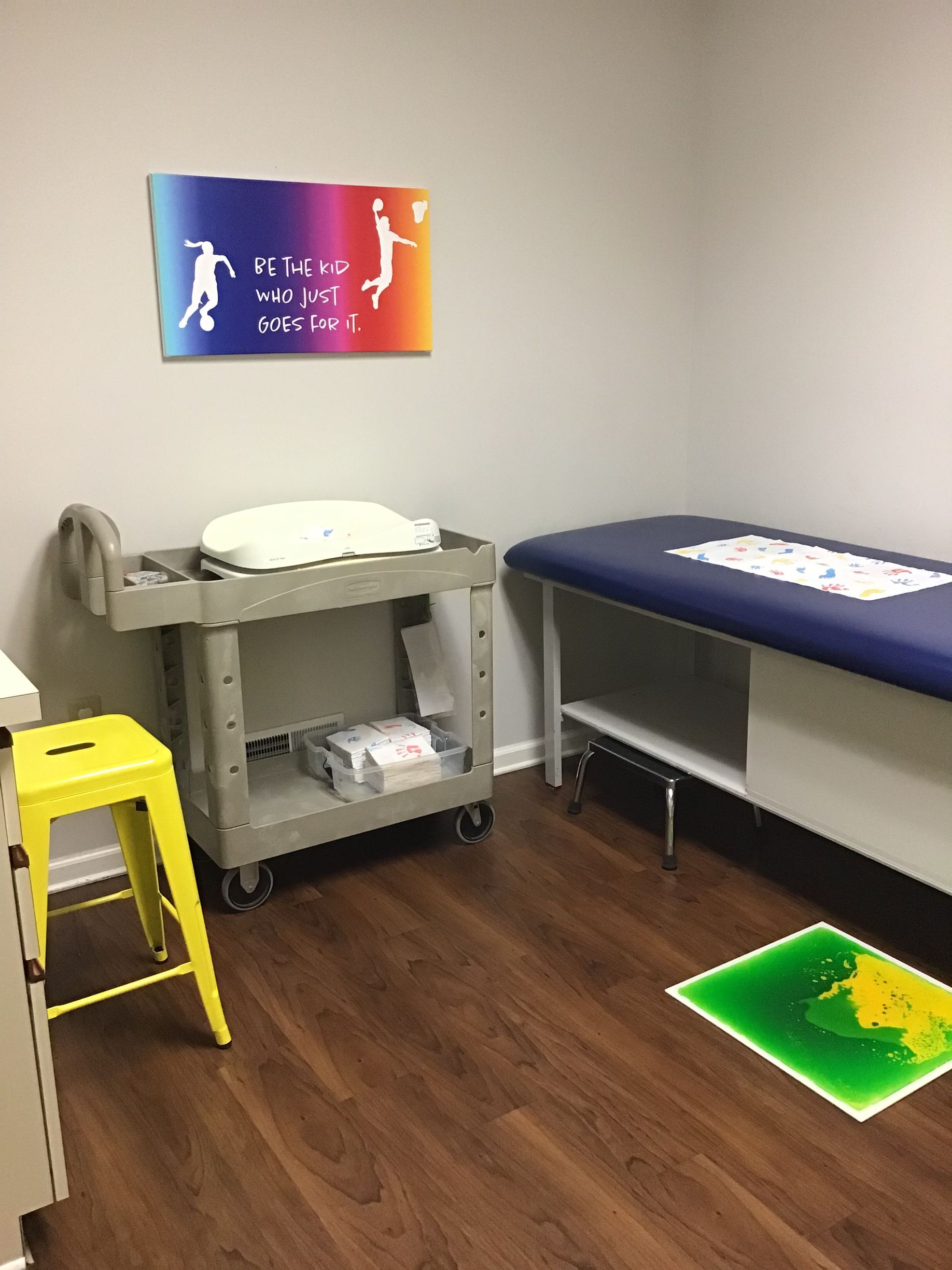 A doctor 's office with a bed , stool , and cart.