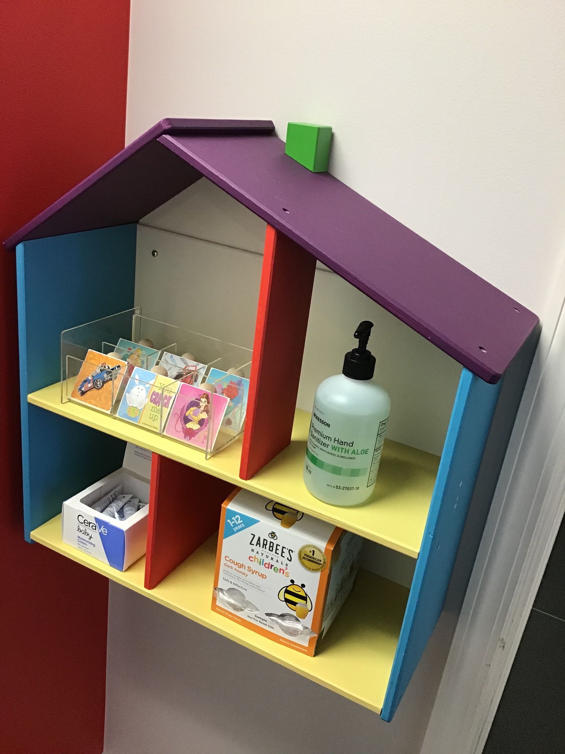 A shelf in the shape of a house with a bottle of hand sanitizer on it.
